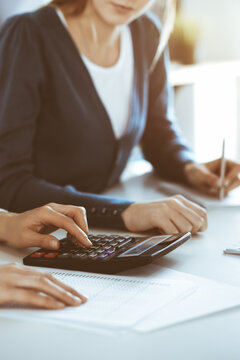 Accountant checking financial statement or counting by calculator income for tax form, hands close-up. Business woman sitting and working with colleague at the desk in office. Audit concept