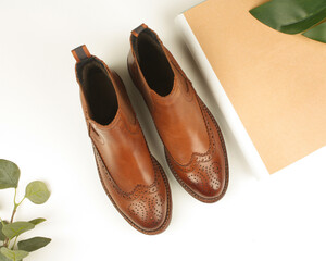 Women's brown shoes with perforations. Chelsea boots, magazine and leaves.