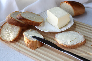  A piece of butter on a white plate, sliced ​​bread. Toast and butter are laid out on a cutting board.