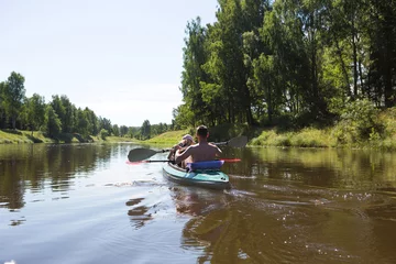 Foto op Canvas A couple of men and women kayak on the river in the summer. Active recreation, family travel, extreme adventure, sports and ecological domestic tourism. Equipment for rafting, boat, oars. © Ольга Симонова