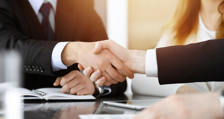 Businessman shaking hands with his colleague above the glass desk in sunny modern office, close-up. Unknown business people at meeting