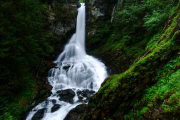 Obraz premium wonderful large soft waterfall between green rocks in the mountains