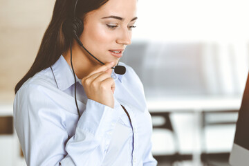 Brunette female customer service representative using headset and consulting clients online. Call center