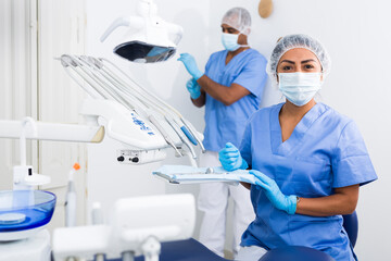 Focused female dentist preparing to receive patients in dental office, checking and arranging tools