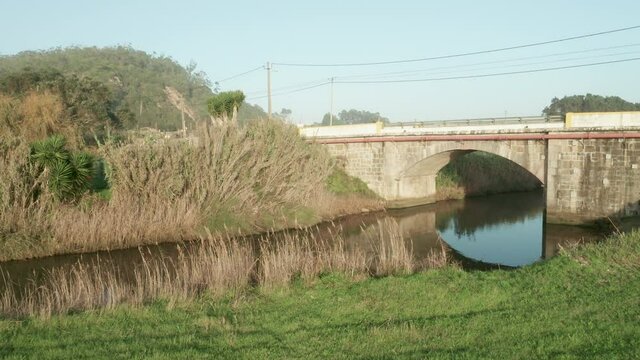 Quiet Lake Among Golden Grass With Arch Bridge In Alcobaca River Near Nazare In Portugal. - Aerial Pullback Shot