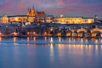 .Charles Bridge on the Vltava River and Prague Castle and the Church of St. Vitus in winter and snow on the roofs in the center of Prague in the early evening