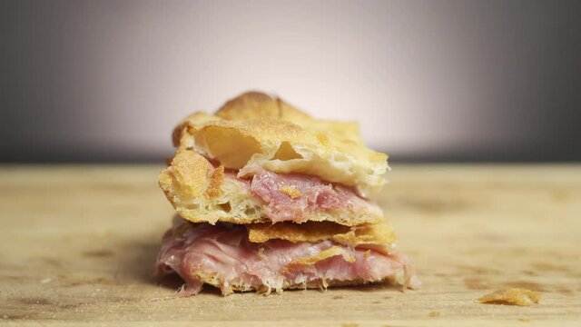 Hands taking a piece of pizza al taglio (pizza by the cut) filled with mozzarella and prosciutto on a wooden board in a cinematic scene