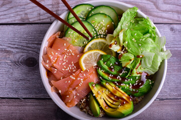 Salmon poke bowl with avocado, cucmber, and lemon on a wood table.