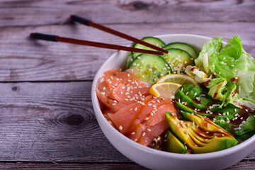 Salmon poke bowl with avocado, cucmber, and lemon on a wood table.