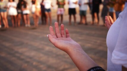 Detail slow-motion shot of the hands of a woman, opened towards the sky, like in a prayer, standing in circle with other people (a spiritual ritual).