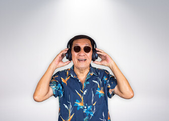 Senior asian man listening to music by headphone, wearing sunglasses on grey background