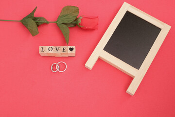 Top view of blackboard with red flower and wooden word love with rings for Valentine's day