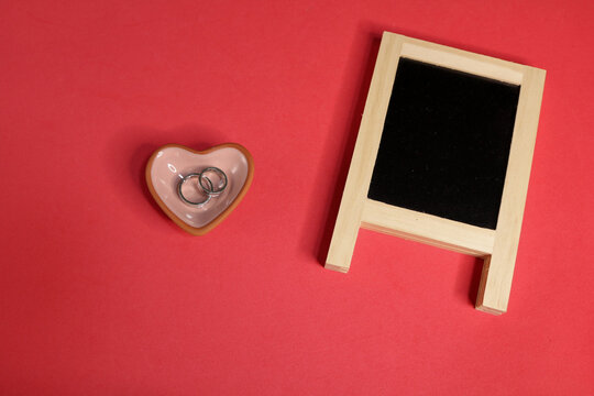 Top view of blackboard and two rings on a heart for Valentine's day on red background