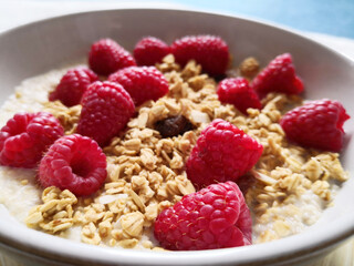 Close up of raspberries in a bowl of oatmeal porridge and granola.