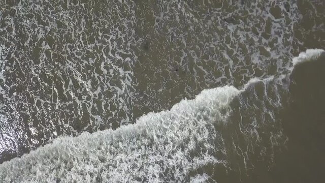 Aerial birds eye view following a wave in the sea