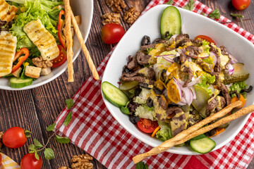 halloumi salad and beef salad in two separate plates on wooden background.