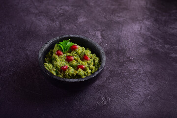 Stone black bowl with spinach and pomegranate seeds appetizer on a dark gray background.
