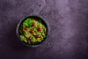 Green pkhali with pomegranate seeds on a dark stone table.