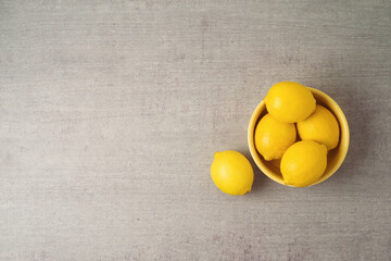 Lemons in yellow bowl over gray background with copy space