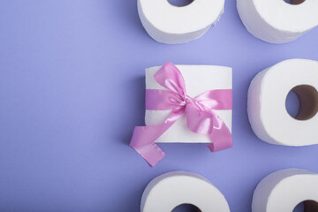 Roll of toilet paper wrapped in a gift bow. on a purple background. top view