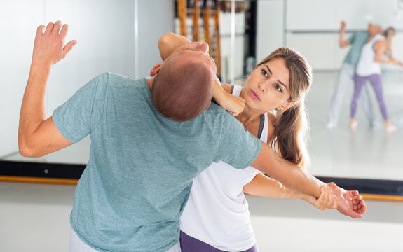 Young woman practicing elbow blow with male partner during self defense course in gym..