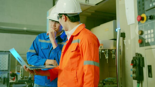 Male Asian engineer professional  having a discussion standing concult cnc machine in the factory ,two asian coworker brainstorm  explaining and solves the process of the cnc operate machine