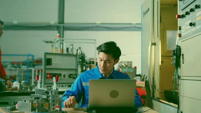 Male Asian engineer professional  having a discussion standing concult cnc machine in the factory ,two asian coworker brainstorm  explaining and solves the process of the cnc operate machine