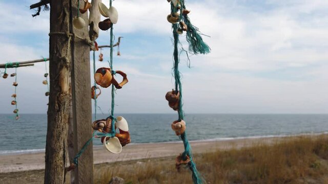 Hanging seashells decoration swang by the wind on wooden beams. Camp at the autumn beach. Sea and blue sky in the background. 