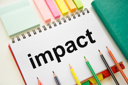 the word impact is written on a white notepad that lies on a white background with colored pencils