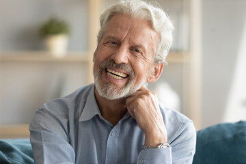 Head shot portrait of happy middle aged older retired man laughing at funny joke. Emotional smiling elderly grandfather looking at camera, enjoying video call or distant communicating with friends.