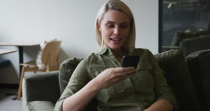 Caucasian businesswoman sitting on couch using a smartphone in modern office
