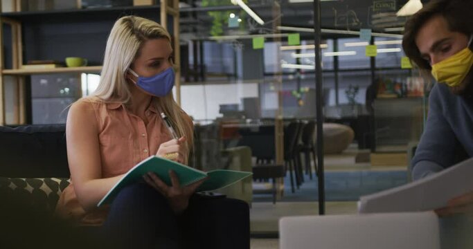 Caucasian business people wearing face masks sitting going through paperwork in modern office