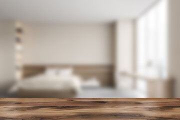 Wooden desk on foreground, blurred beige bedroom with furniture
