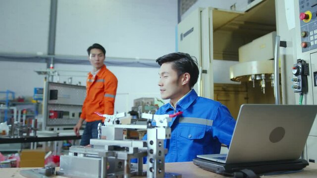 Male Asian engineer professional  having a discussion standing concult cnc machine in the factory ,two asian coworker brainstorm  explaining and solves the process of the cnc operate machine