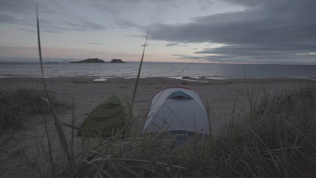 Wild camping in a beach in scotland. Two tents in fornt of the sea during sunrise time. Wide angle shot and green vegetation