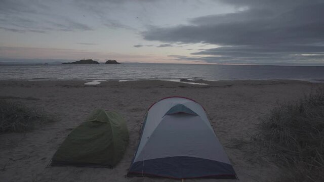 Wild camping in a beach in scotland. Two tents in fornt of the sea during sunrise time. Wide angle shot.