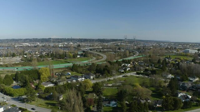 Flying upward with drone filming sprawling suburbia with highway and bridge in background near Surrey BC.