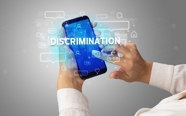 Female hand typing on smartphone with DISCRIMINATION inscription, social media concept