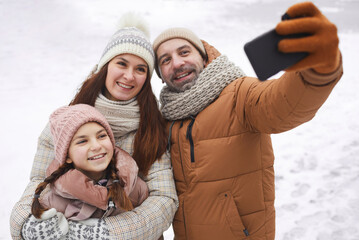 High angle portrait of happy family taking selfie photo while enjoying walk outdoors together in winter forest