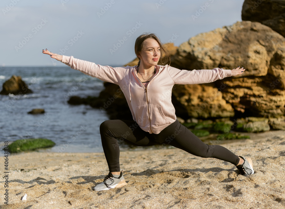 Wall mural Fitness woman practicing yoga asana poses on the wild beach. Warrior 2