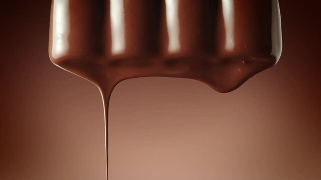 Melted chocolate dripping from a chocolate bar over a dark brown background, vertical camera movement. Chocolate dessert. Confectionery concept backdrop.