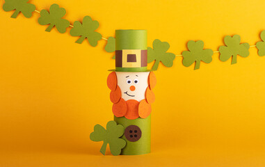 Leprechaun made of handmade paper with green four-leaf clover on the background