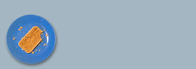 Banner with single piece of bread with a bitten mark lies on a blue plate at solid light blue color background with copy space for text. Concept of poverty, misery and malnutrition.
