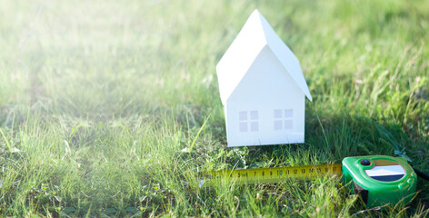 Miniature paper house on green grass in summer. Mortgage. Measuring tape or tape measure. The...