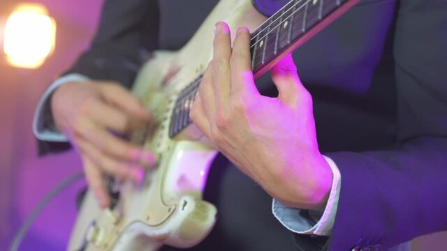 Close up of a professional musician playing chords on an electric stratocaster guitar during a live session on stage with warm studio lights in the blurred background. Shot in 4K.