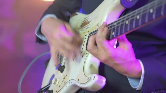 Close up of a professional musician playing fast chords on an electric stratocaster guitar during a live session on stage with warm studio lights in the blurred background. Shot in 4K.