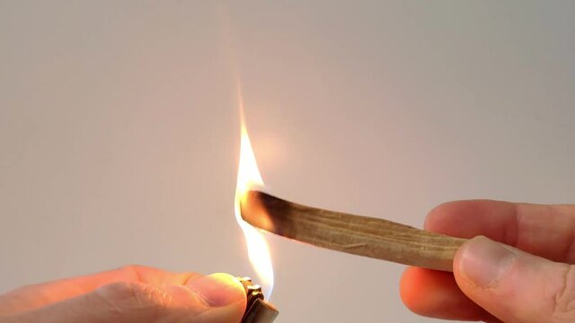 A Palo Santo stick is light up with a lighter. A big flame starts to grow on the sitck and is then turned off by shaking the stick. The smoke which is used as air freshner starts to spread around.