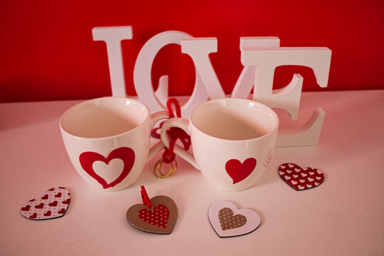 cups with hearts joined rings, red ribbon and love word white