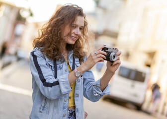 Cheerful curly hair woman tourist with retro camera walking along city street on bright sunny day. Travel concept