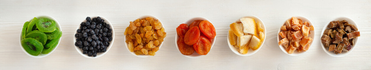 On the side of the plates with different dried fruits and candied fruit on a white wooden background. Extra wide banner. Winter healthy sweets. Winter vitamins. Vegan sweets. 
